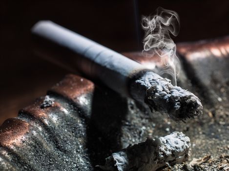 Closeup of cigarette on ashtray with a beautiful wisp of smoke on a dark background