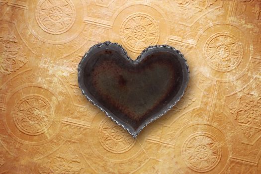 Photo of a metal heart on top of a vintage tattered wallpaper background.
