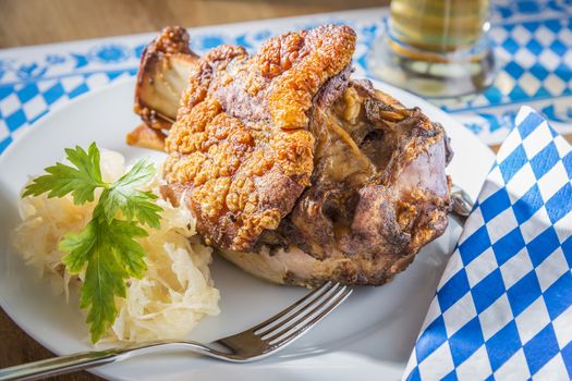 Oktoberfest pork hock with cabbage on a table with beer and Bavarian white blue napkin and fork