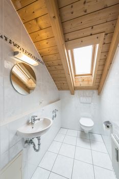 picture of a white tiled restroom with tiolet, basin, mirror and light.