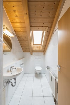 Picture of a white tiled restroom with basin, toilet, mirror, light and window