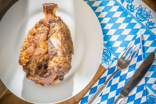 Oktoberfest pork hock on a table with Bavarian white bluw napkin and fork with knife