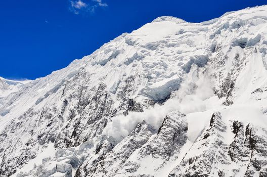 Avalance falling from snowy frozen mountain peak with glacier