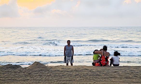 Horizontal color landscape of an Asian Indian family down on the beach early to catch the sunrise and family photographs. Man, woman and two kids captured at Manaputti Beack, Pondicherry, India