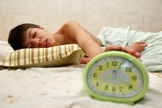 Sleeping boy and alarm clock in the bedroom