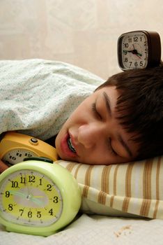 Pretty sleeping boy and his three alarm-clocks