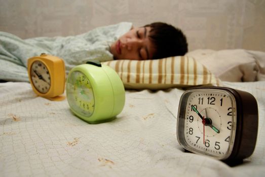 Sleeping boy at the morning and three alarm-clocks