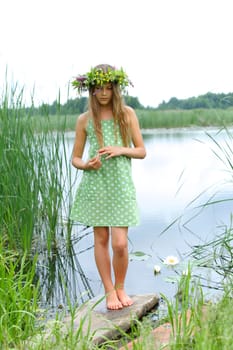 Spring beautiful girl with wreath of flowers near forest lake