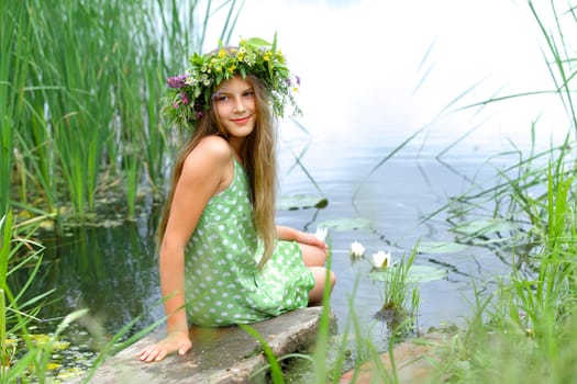 Spring beautiful girl with wreath of flowers near forest lake