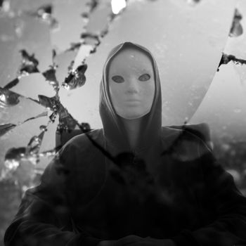 Masked figure reflected through broken glass mirror. Black and white.
