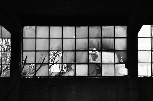 Broken windows and concrete wall in abandoned factory. Black and white.