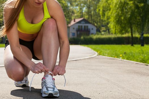 Beautiful young woman in fitness wear ties shoelaces outdoors