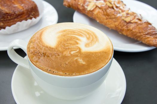 Cup of Caffe Latte with Almond Croissant Pastry in Background