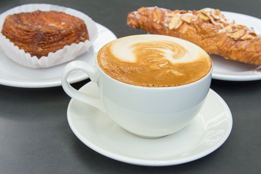 Cup of Caffe Latte with Almond Croissant and Flaky Pastry in Background