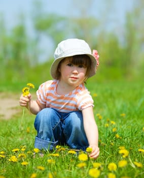 Sweet beautiful girl sitting on a green meadow with dandelions