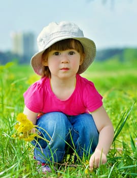 Sweet beautiful girl sitting on a green meadow with dandelions