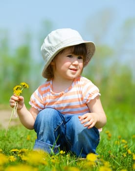 Sweet beautiful girl sitting on a green meadow with dandelions