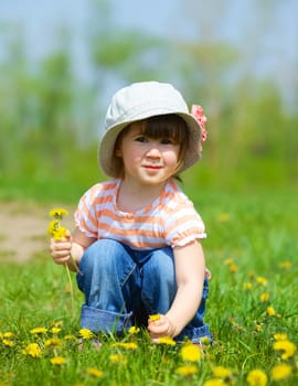 Sweet beautiful girl sitting on a green meadow with dandelions