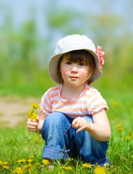 Sweet beautiful girl sitting on a green meadow with dandelions