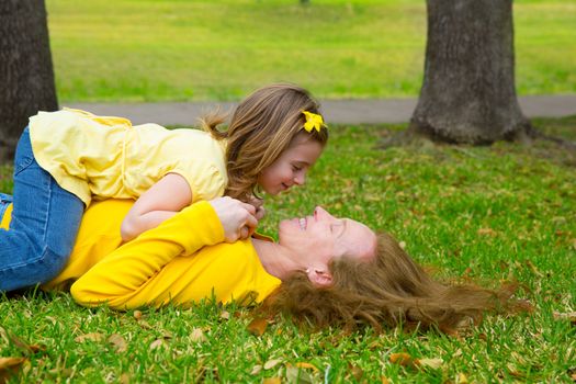 Daughter and mother playing lying on park lawn outdoor dressed in yellow