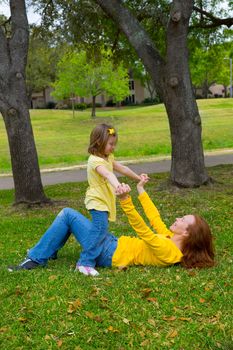 Daughter and mother playing lying on park lawn outdoor dressed in yellow