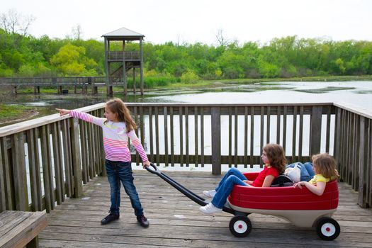 children girls looking and pointing at park lake with outdoor dump cart
