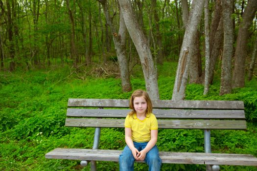 blond lonely children girl happy sitting on park bench on forest jungle