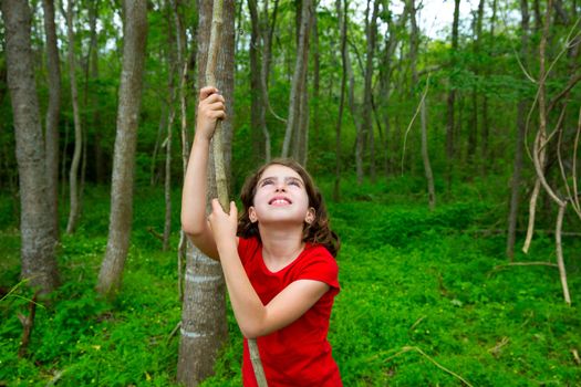 Happy kid girl playing in forest park jungle with liana looking up