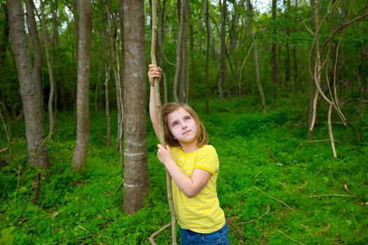 Happy kid girl playing in forest park jungle with liana looking up