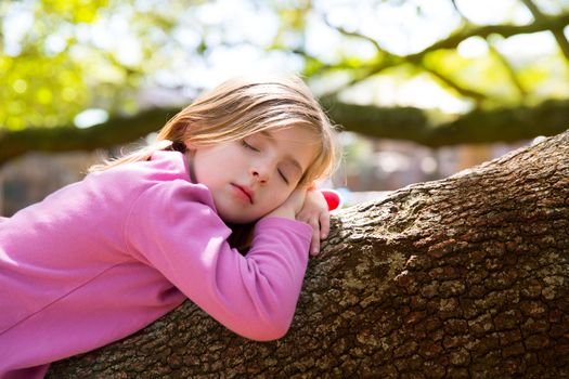 Blond children kid girl having a nap lying on a tree branch