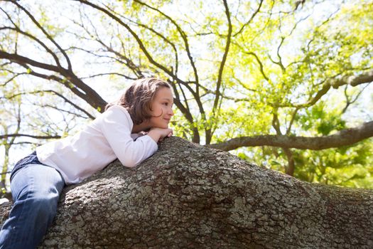 Beautiful children kid girl resting lying on a tree branch