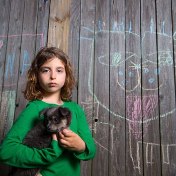 children girl holding puppy dog after chalk painting on backyard wood fence