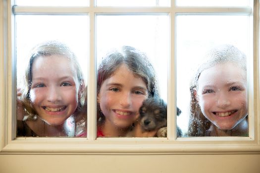 three sister friends looking through the window with a pup and raindrops