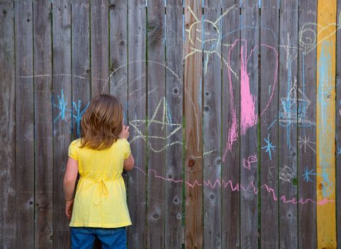 Blonk kid girl playing with drawing chalks in the backyard wooden fence