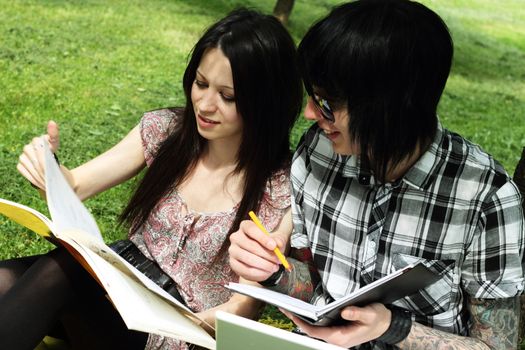 Couple of young students studying outdoors with laptop and books