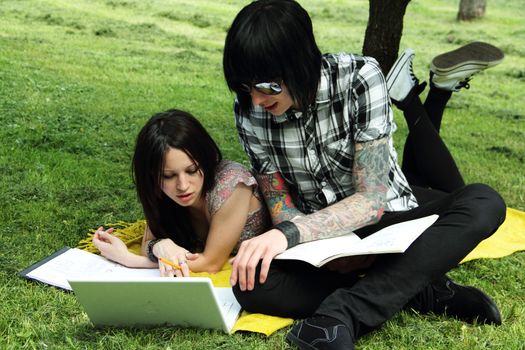 Couple of young students studying outdoors with laptop and books