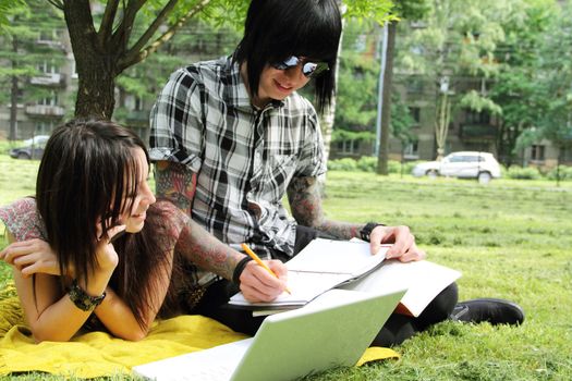 Couple of young students studying outdoors with laptop and books