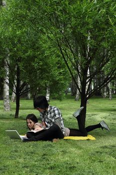 Couple of young students studying outdoors with laptop and books