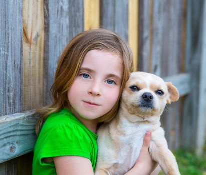 Blond happy girl with her chihuahua doggy portrait on backyard fence