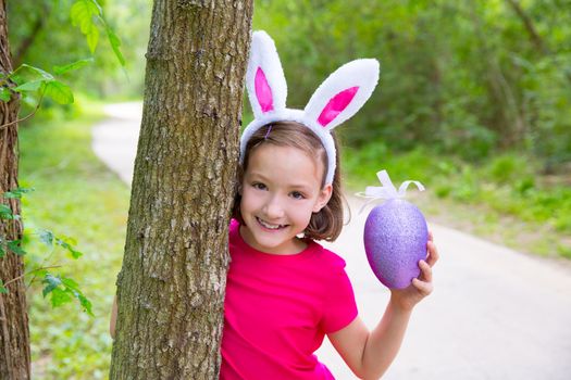 Easter girl with big purple egg and funny bunny ears on the forest