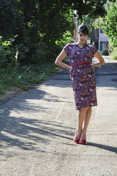 Young fashionable woman wearing a multi colored flower pattern dress standing in an urban alley