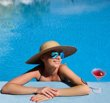 Woman in hat relaxing at the pool with cosmopolitan cocktail