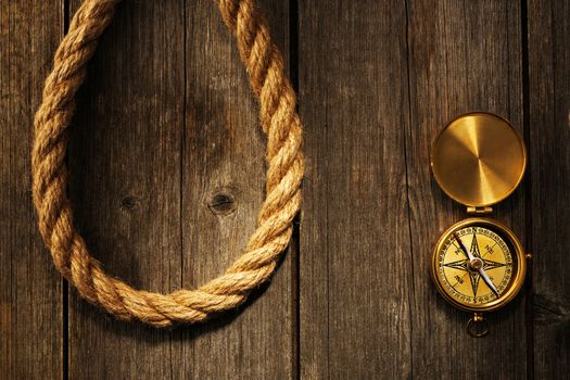 Antique brass compass and rope over wooden background