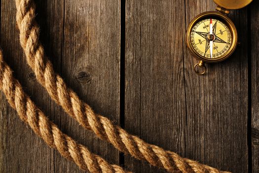 Antique brass compass and rope over wooden background