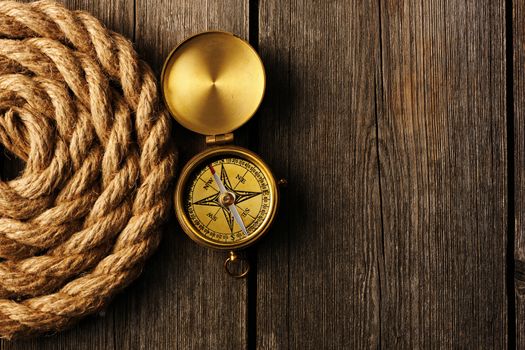 Antique brass compass and rope over wooden background
