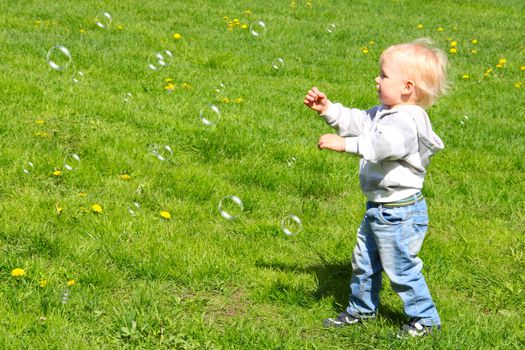 Little child catching soap bubbles on green grass