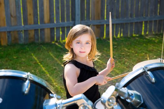 Drummer blond kid girl playing drums in tha backyard lawn