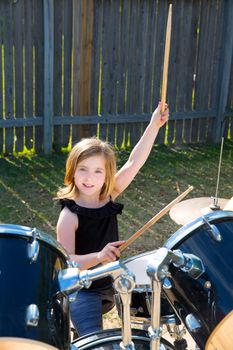 Drummer blond kid girl playing drums in tha backyard lawn