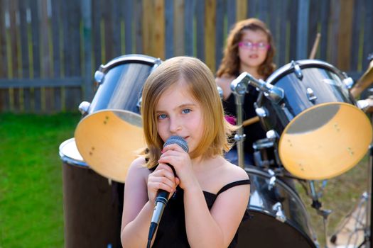 Blond kid girl singing in tha backyard with drums behind
