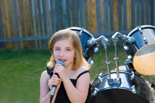 Blond kid girl singing in tha backyard with drums behind